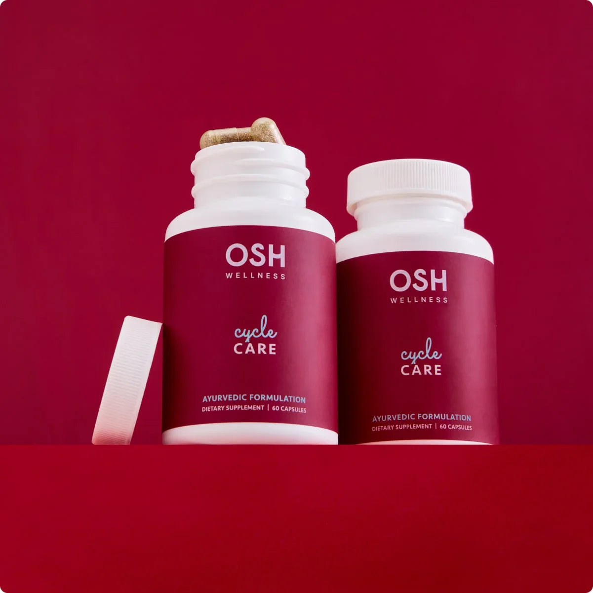 Two bottles of OSH Wellness cycle care capsules against a red background.