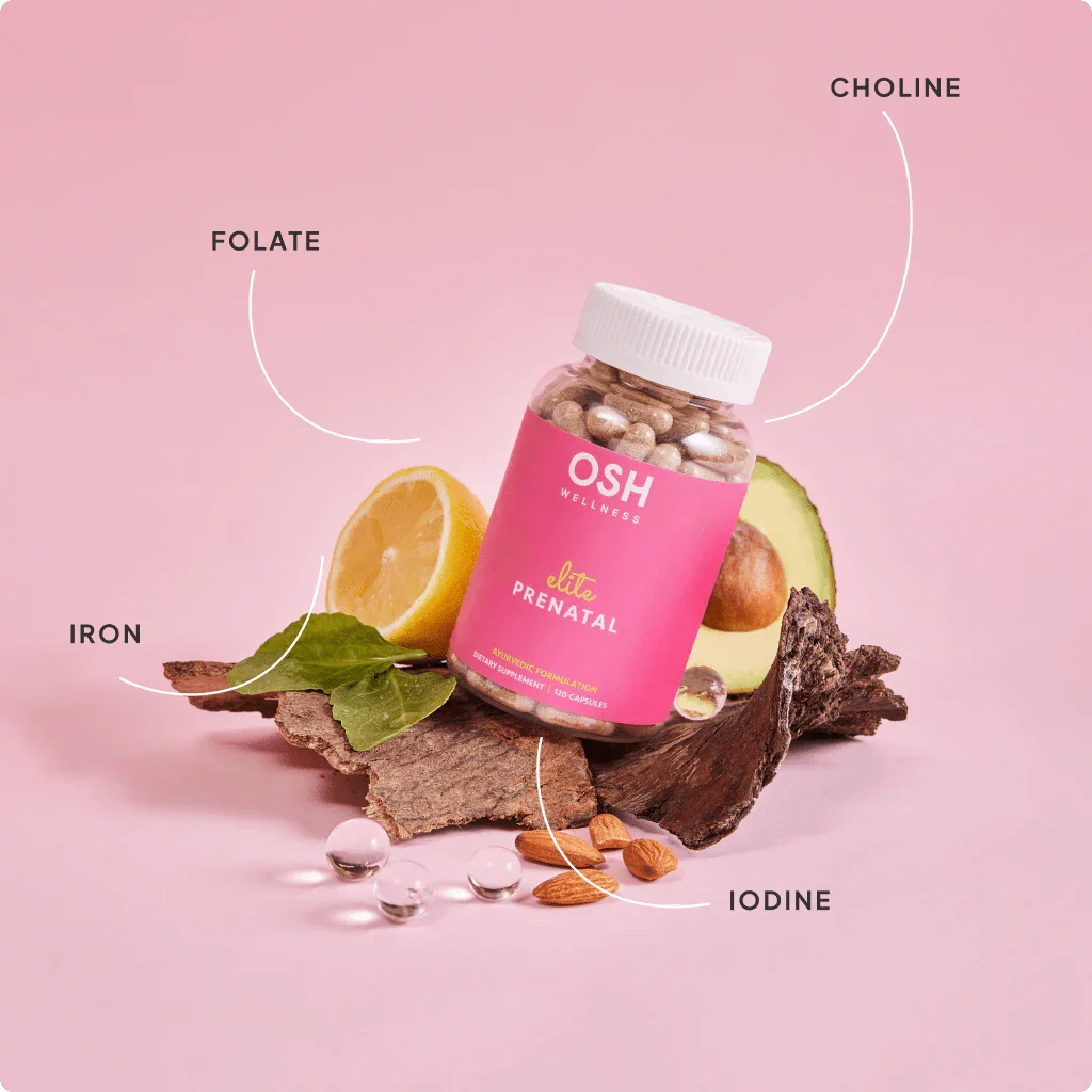 Close-up of prenatal supplement bottle amid various foods, including lemons, almonds, and avocado on wooden surface.