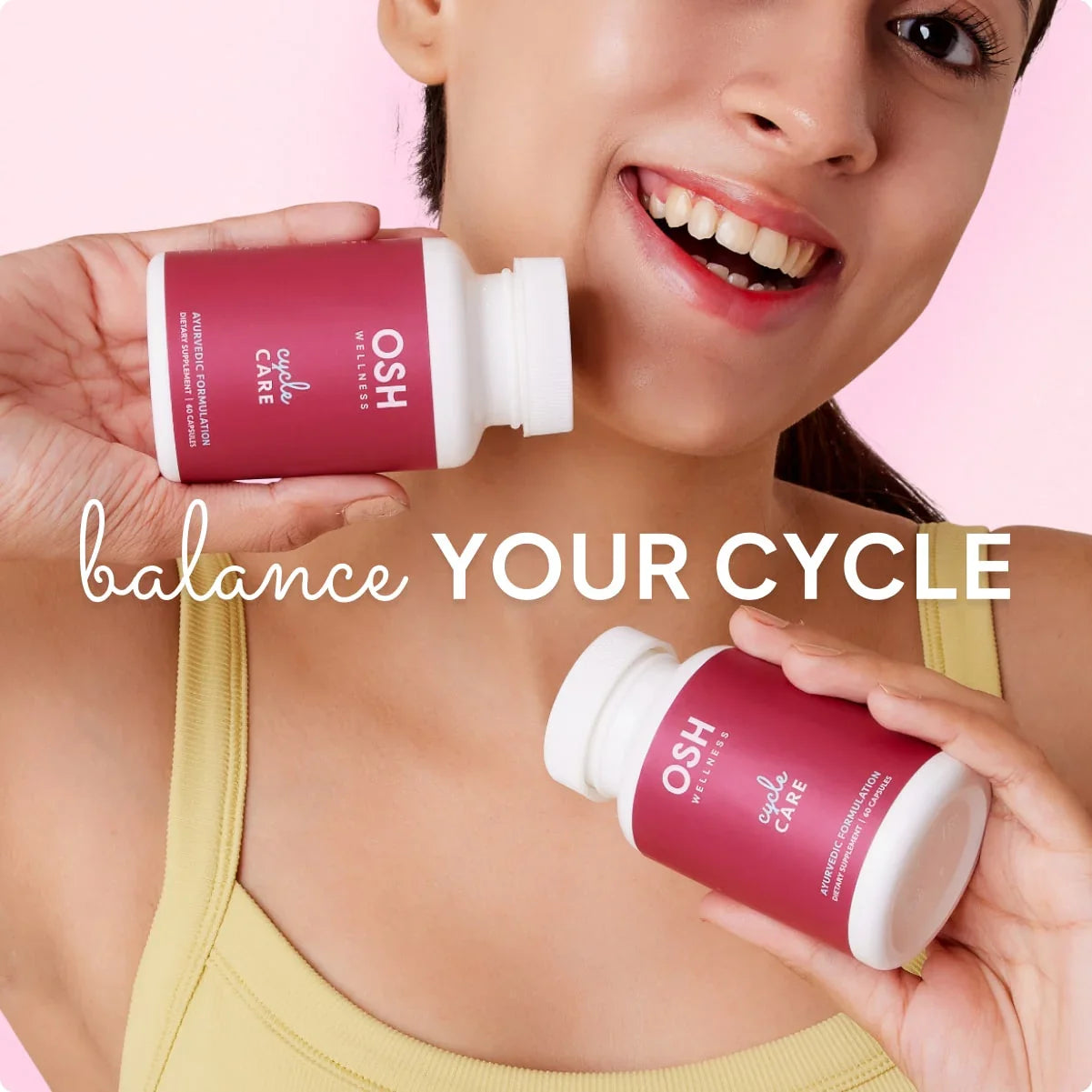 A smiling woman holding two bottles of OSH Wellness Cycle Care dietary supplements in front of a pink backdrop.