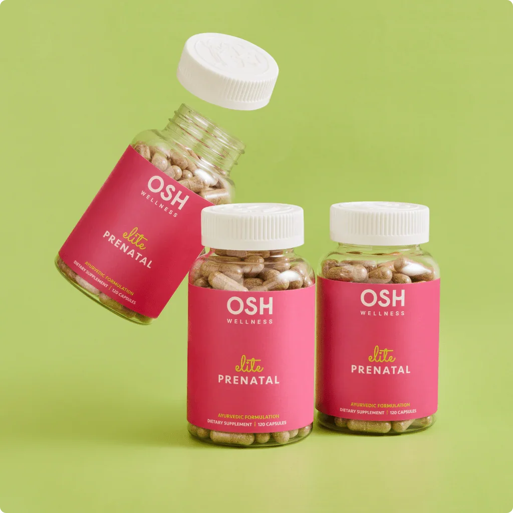 Three bottles of OSH Wellness Elite Prenatal dietary supplement capsules with pink labels and white caps on a light green background. One bottle is slightly tilted in mid-air with its cap floating above it. The other two bottles stand upright.